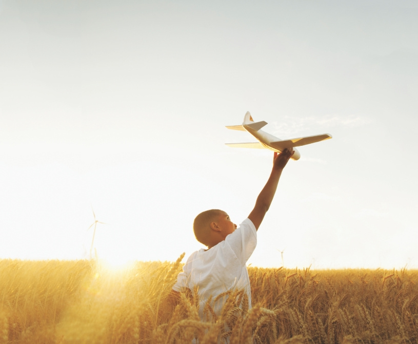 A child playing with a toy plane in a vast field