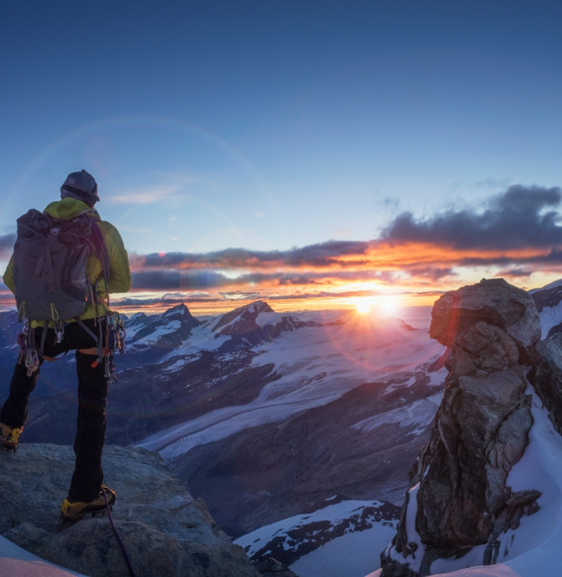 Een bergbeklimmer die op de top van een berg kijkt naar een zonsondergang